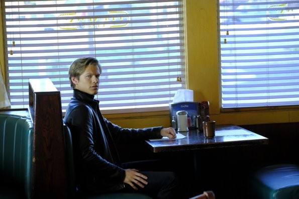 Mac (Lucas Till) est assis à une table dans un restaurant.