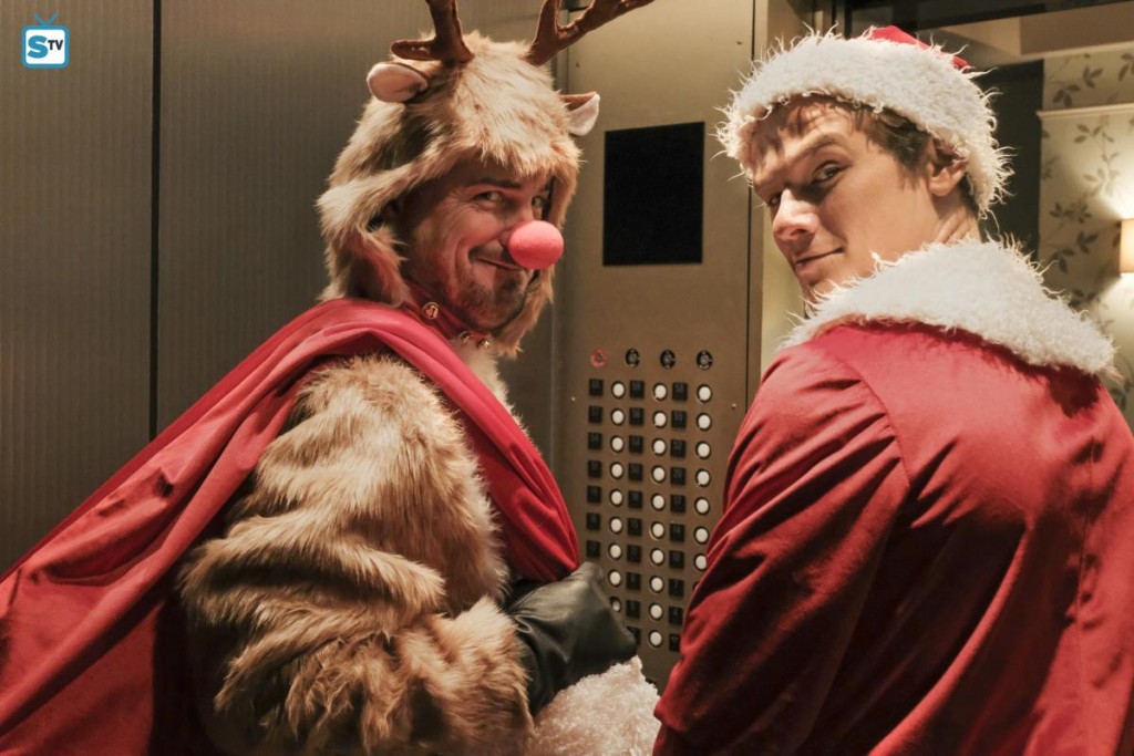 Jack (George Eads) et Mac (Lucas Till) sont vêtus d'un costume de Noël et se trouvent dans un ascenseur.