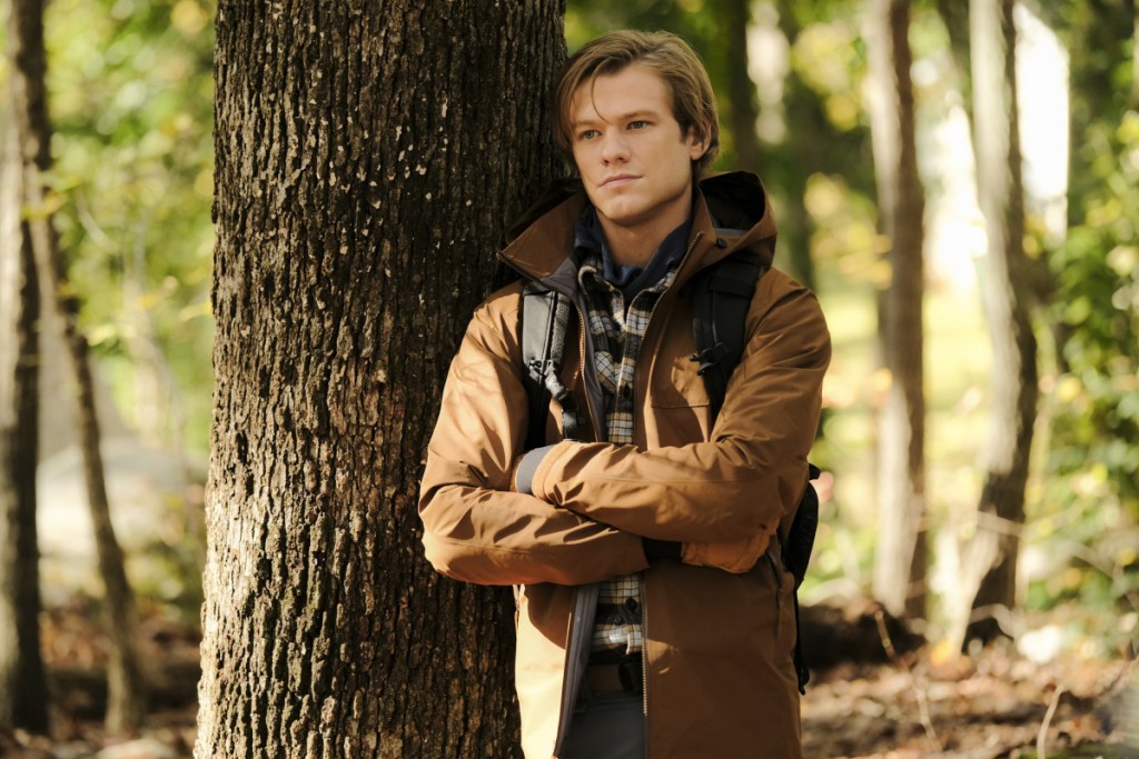 Mac (Lucas Till) est posé contre un arbre et semble perdu dans ses pensées.