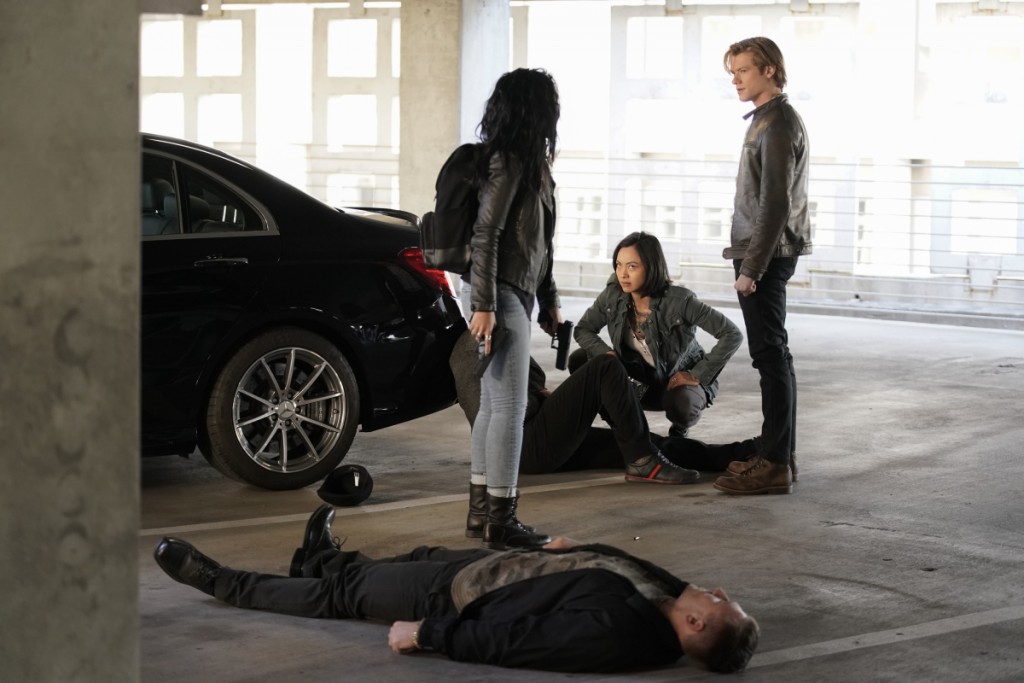 Riley (Tristin Mays), Desi (Levy Tran) et Mac (Lucas Till) se trouvent sur un parking avec deux criminels alongés sur le sol.