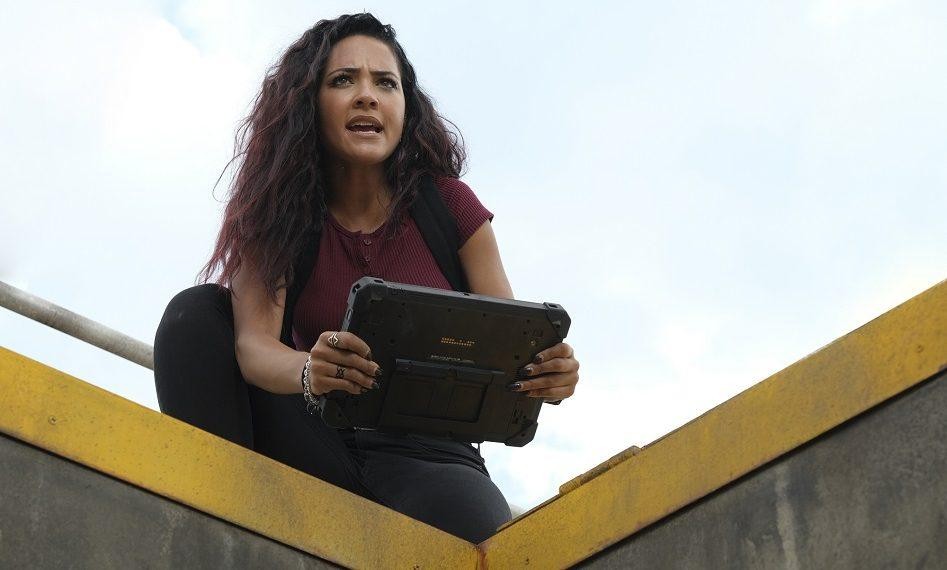 Riley (Tristin Mays) se trouve sur le terrain et tient une tablette entre ses mains.