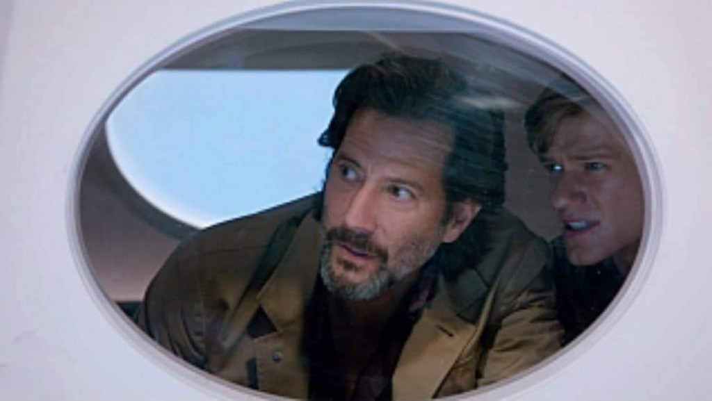 Russ (Henry Ian Cusick) et Mac (Lucas Till) regardent par le hublot d'un avion.