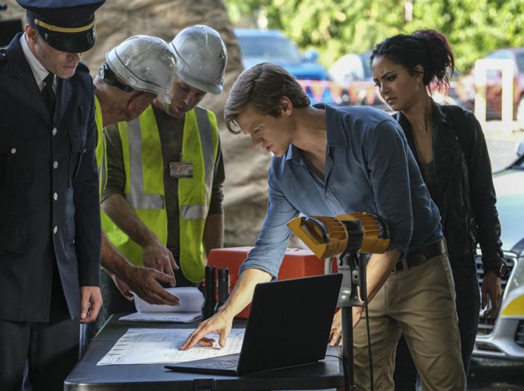 Mac (Lucas Till) observe le plan du bâtiment avec Riley (Tristin Mays) afin de venir en aide aux survivants.