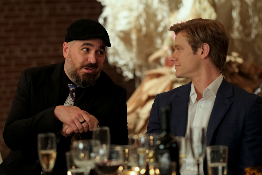 MacGyver (Lucas Till) discute avec un homme au cours du repas.