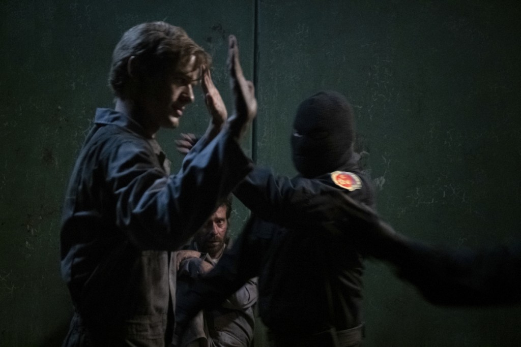 Alors qu'il lève les mains en l'air, Mac (Lucas Till) est emmené par deux personnes cagoulés.