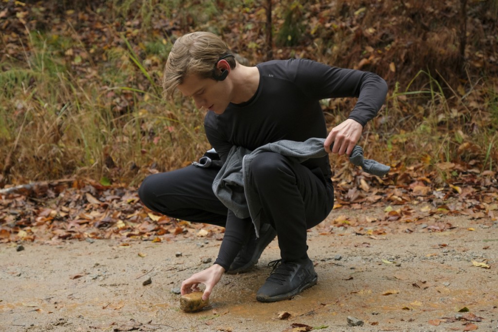 MacGyver (Lucas Till) ramasse une pierre afin de fabriquer quelque chose.