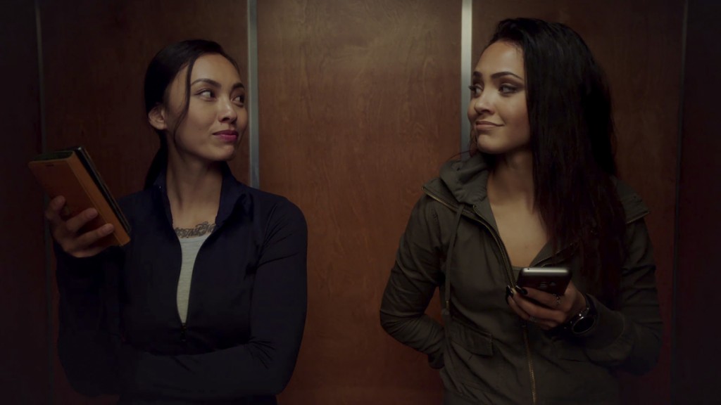 Desi (Levy Tran) et Riley (Tristin Mays) se trouvent dans un ascenseur et se regardent mutuellement.