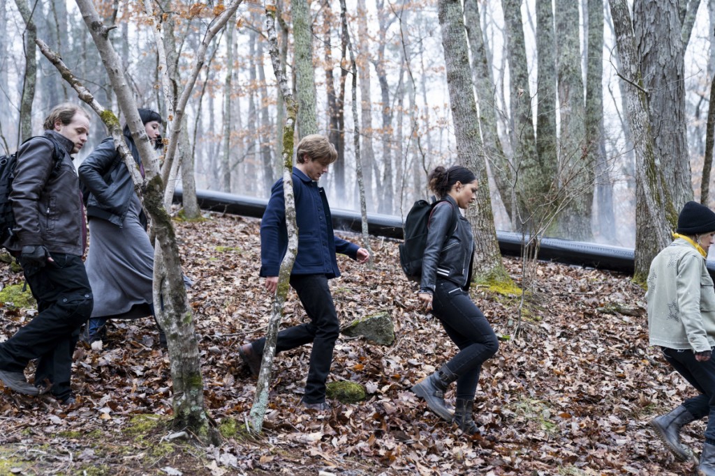 Mac (Lucas Till) et Riley (Tristin Mays) marchent dans une forêt avec plusieurs manifestants.