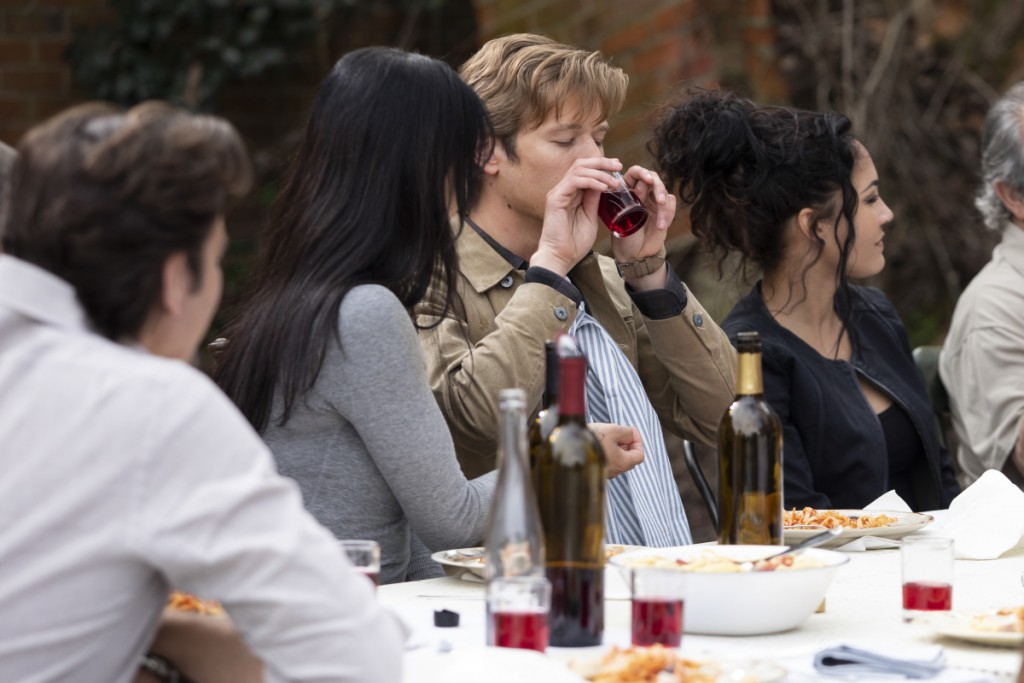 Mac (Lucas Till) est en train de boire un verre de vin sous le regard de Desi (Levy Tran).