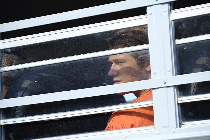 MacGyver (Lucas Till) est assis dans un bus de prisonniers.
